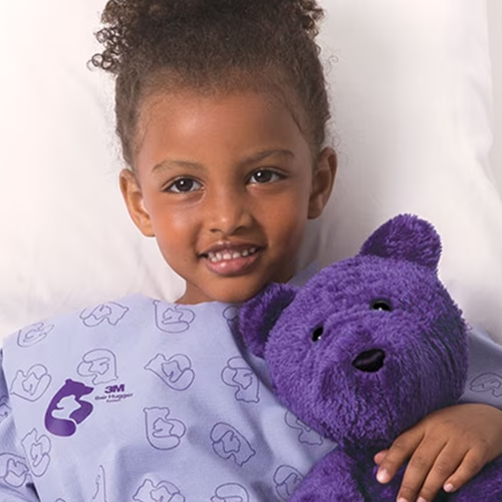 Young girl in hospital bed with purple teddy bear.